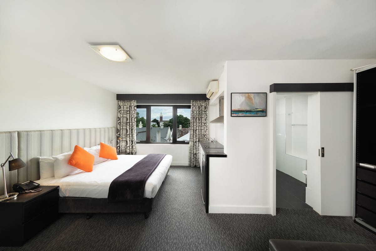 Una habitación de hotel con cama, escritorio, ventana con cortinas, un cuadro y una puerta.