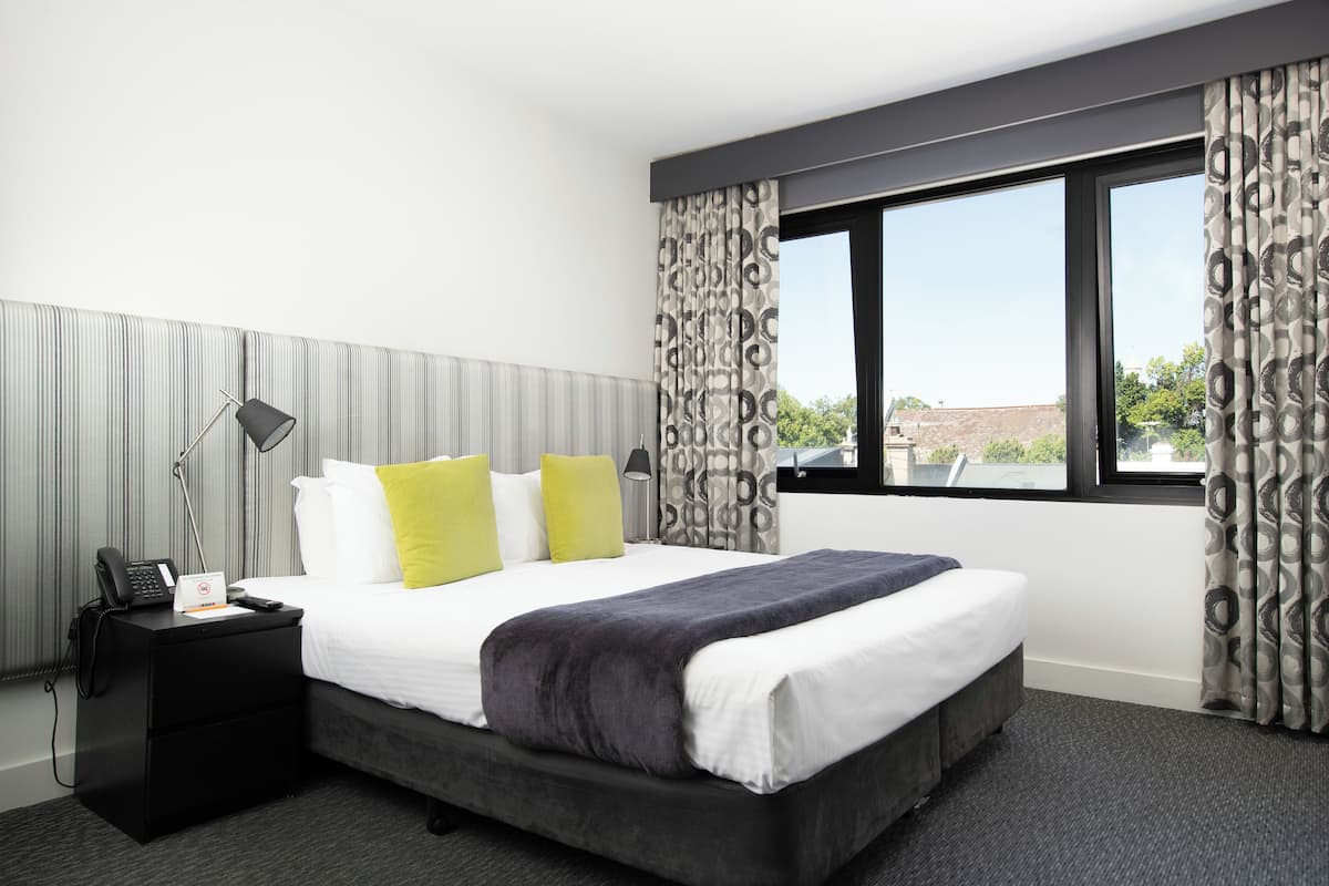 Una habitación de hotel con una cama grande, una mesita de noche con un teléfono y una ventana con cortinas.