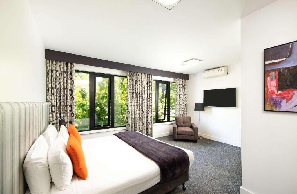Una habitación de hotel moderna con una cama grande, una silla, un televisor de pantalla plana y un cuadro en la pared.