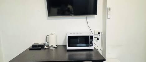 Een kleine kamer met een bureau, een televisie, een magnetron, een minibar en een stoel.