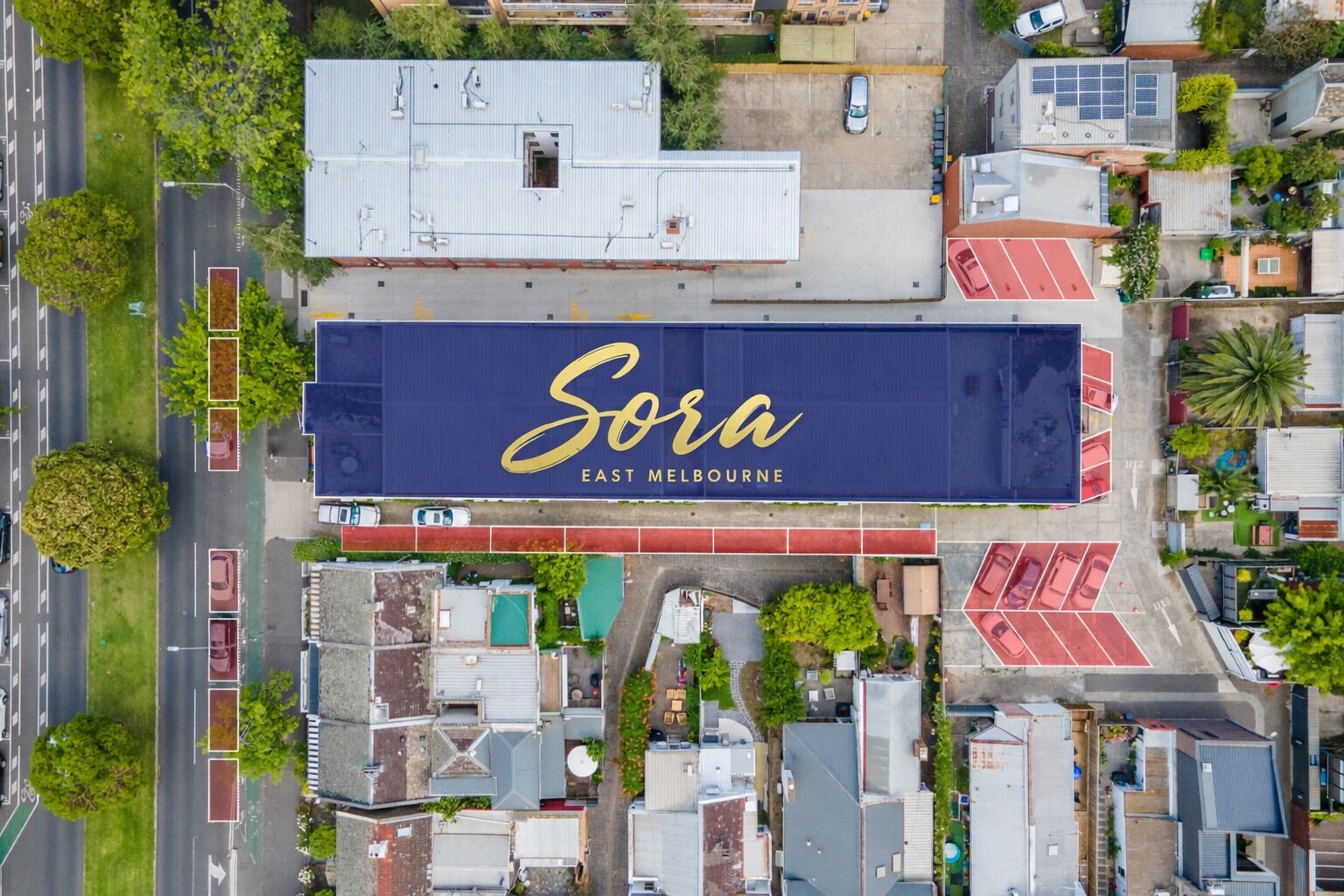 Vista aérea de um edifício com a sinalização 'Sora East Melbourne', cercado por outros edifícios e um estacionamento.