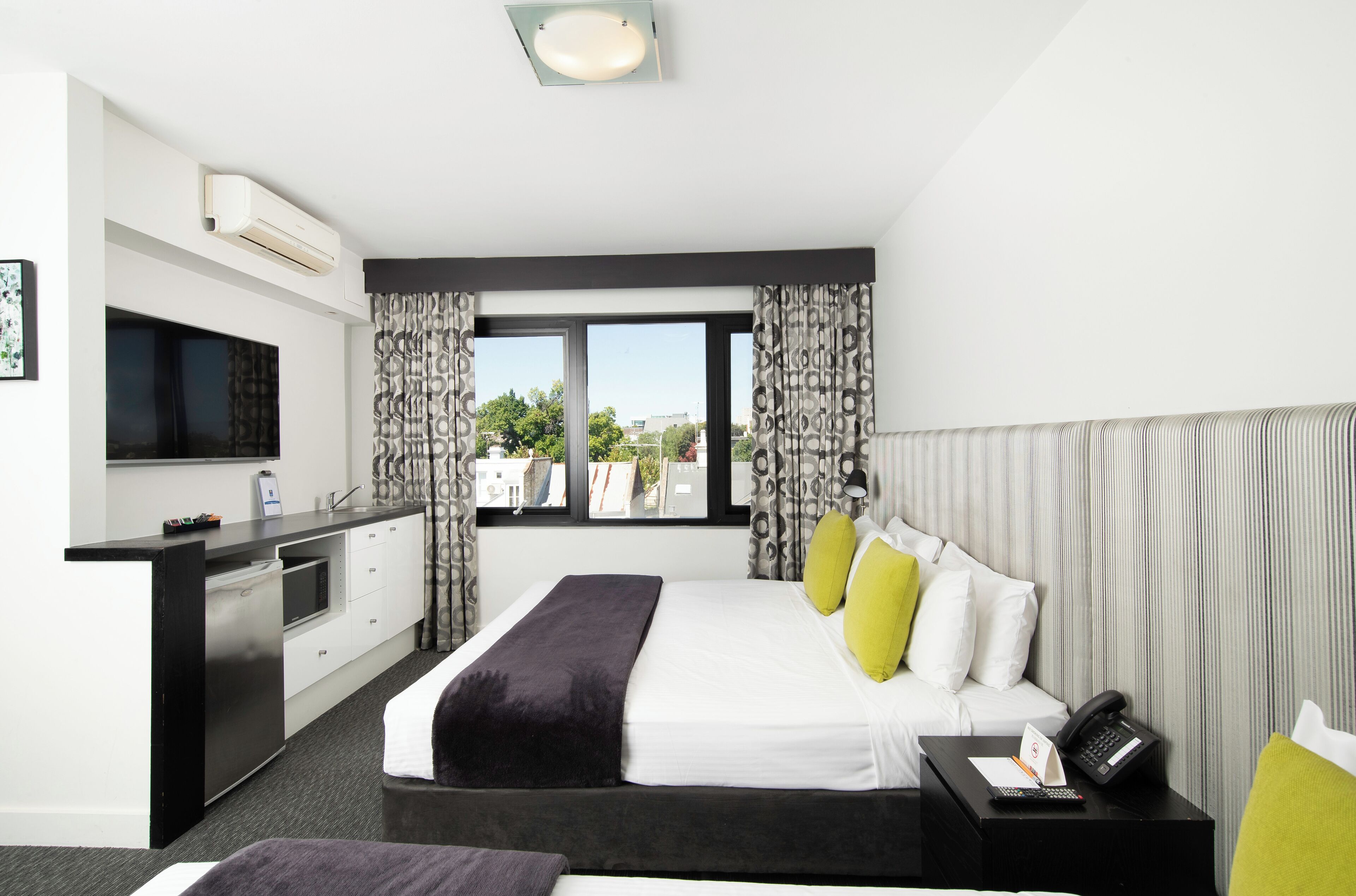 A hotel room with a bed, bedside table, desk, and a TV.