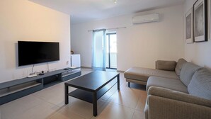 A modern living room with a flat-screen TV, a dark coffee table, and a grey sofa. - 3BR Central with Balcony - Sliema Area (Pembroke)
