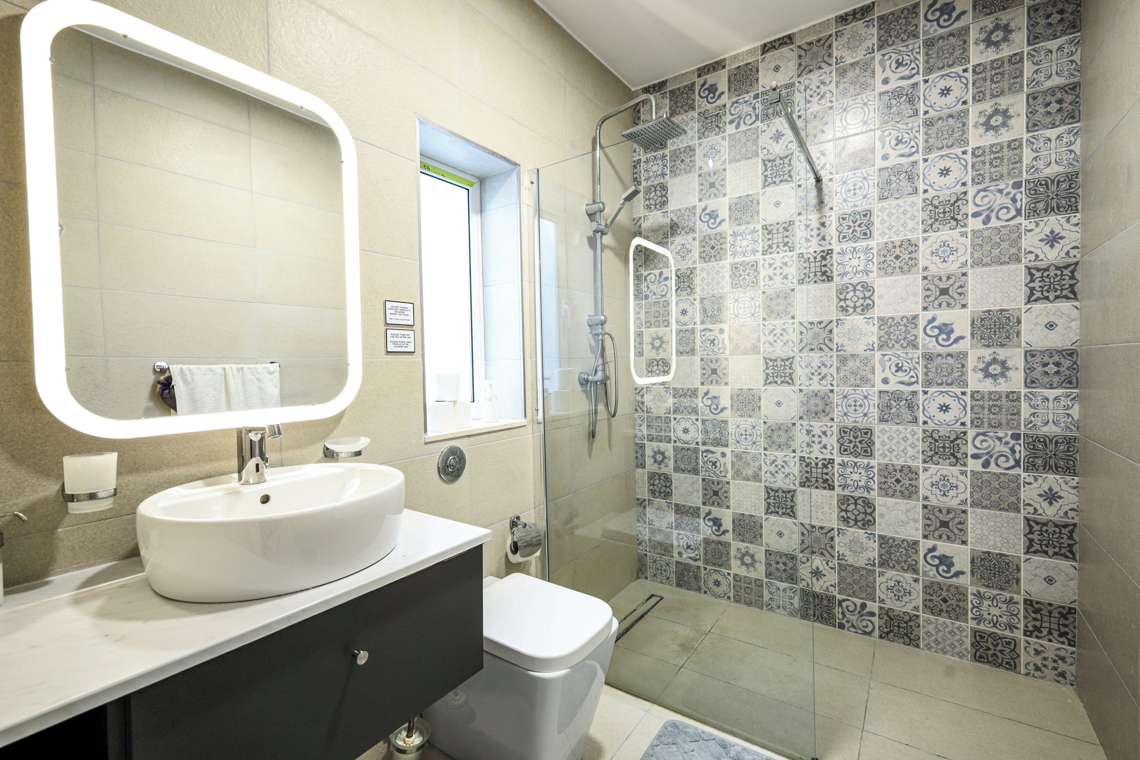 A bathroom with a white sink, a toilet, a shower with a glass door, and a tiled wall with a decorative pattern.