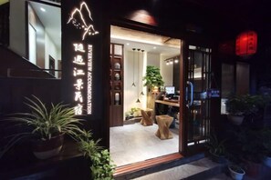 A hotel entrance with a reception desk, seating area, and potted plants. - Phoenix Suiyu Riverview Homestay (North Gate Chenglou Branch) (Fenghuang)