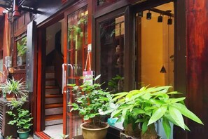 A wooden building with a staircase leading to an upper level, potted plants outside, and a door with a sign. - Phoenix Suiyu Riverview Homestay (North Gate Chenglou Branch) (Fenghuang)
