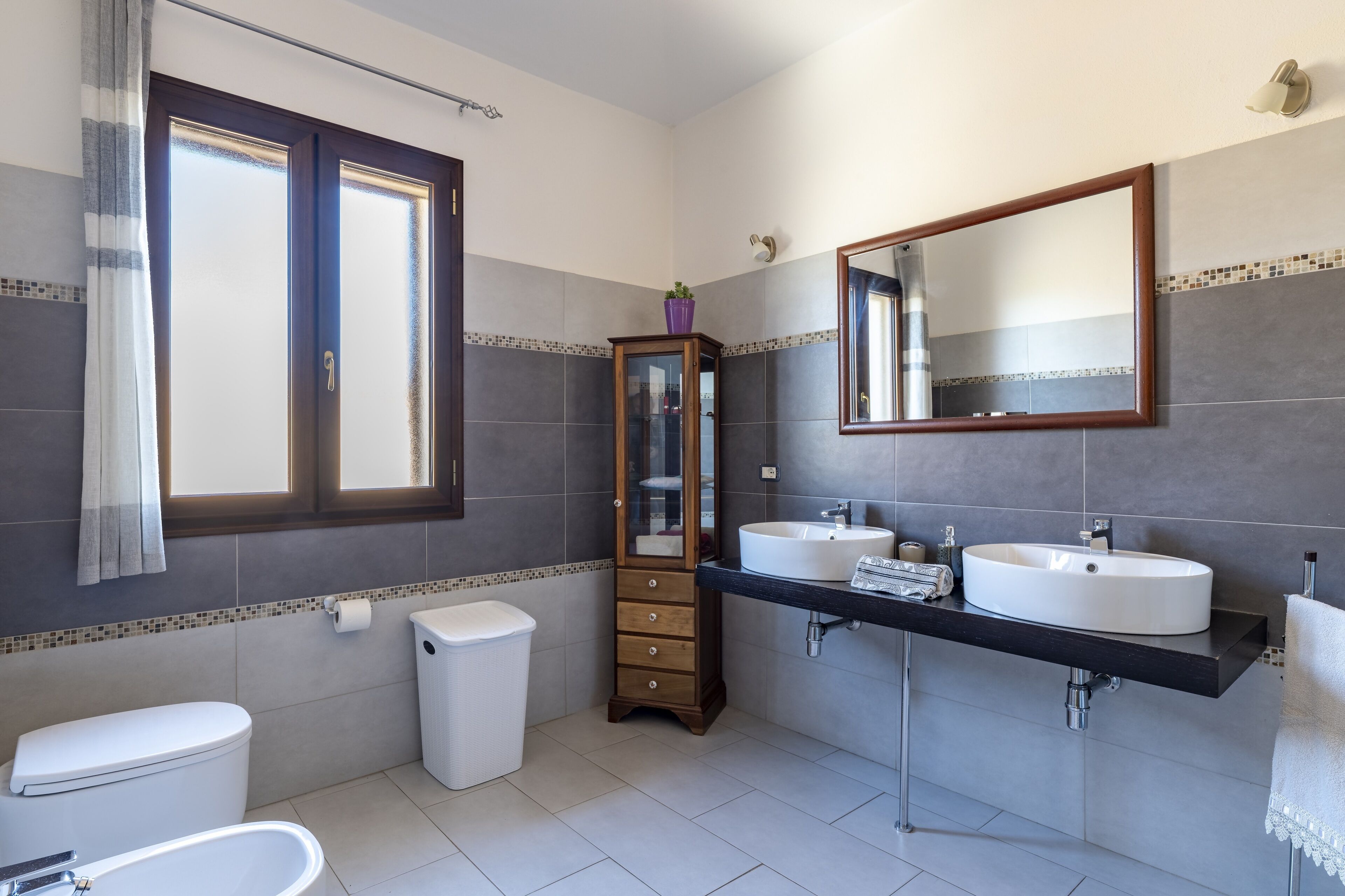 A modern bathroom with two sinks, a toilet, a bathtub, a cabinet, and a large mirror.