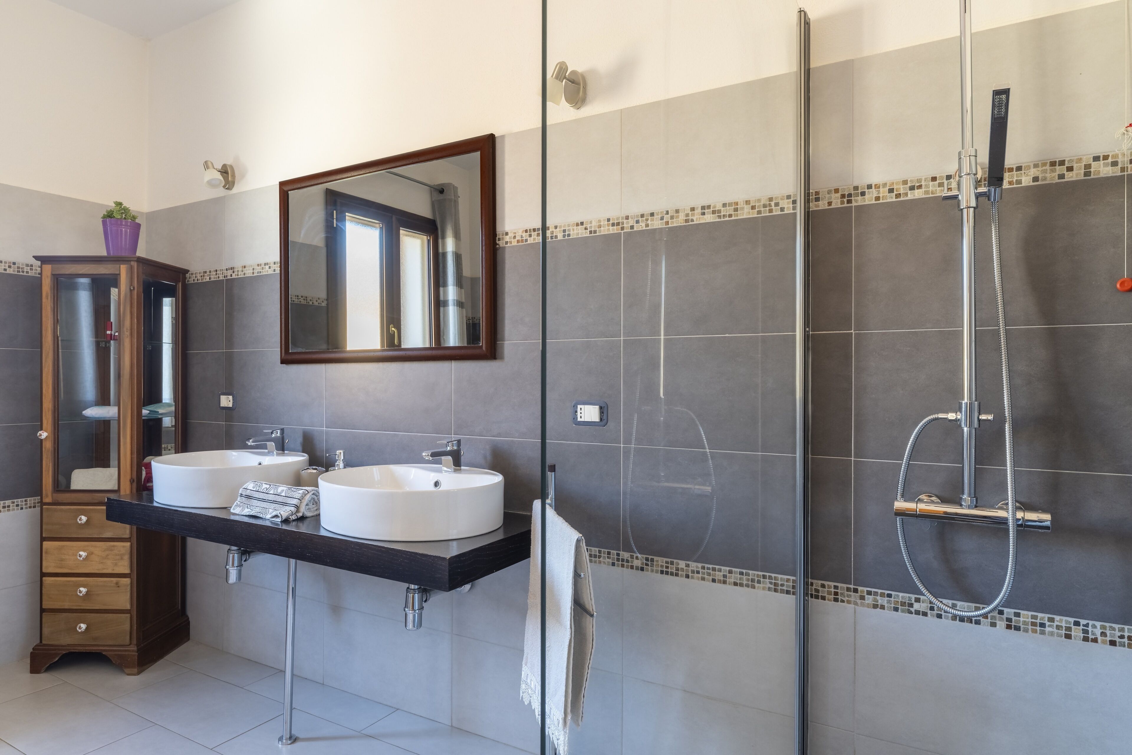 Un baño moderno con dos lavamanos, un espejo grande y cabina de ducha con paredes de cristal.