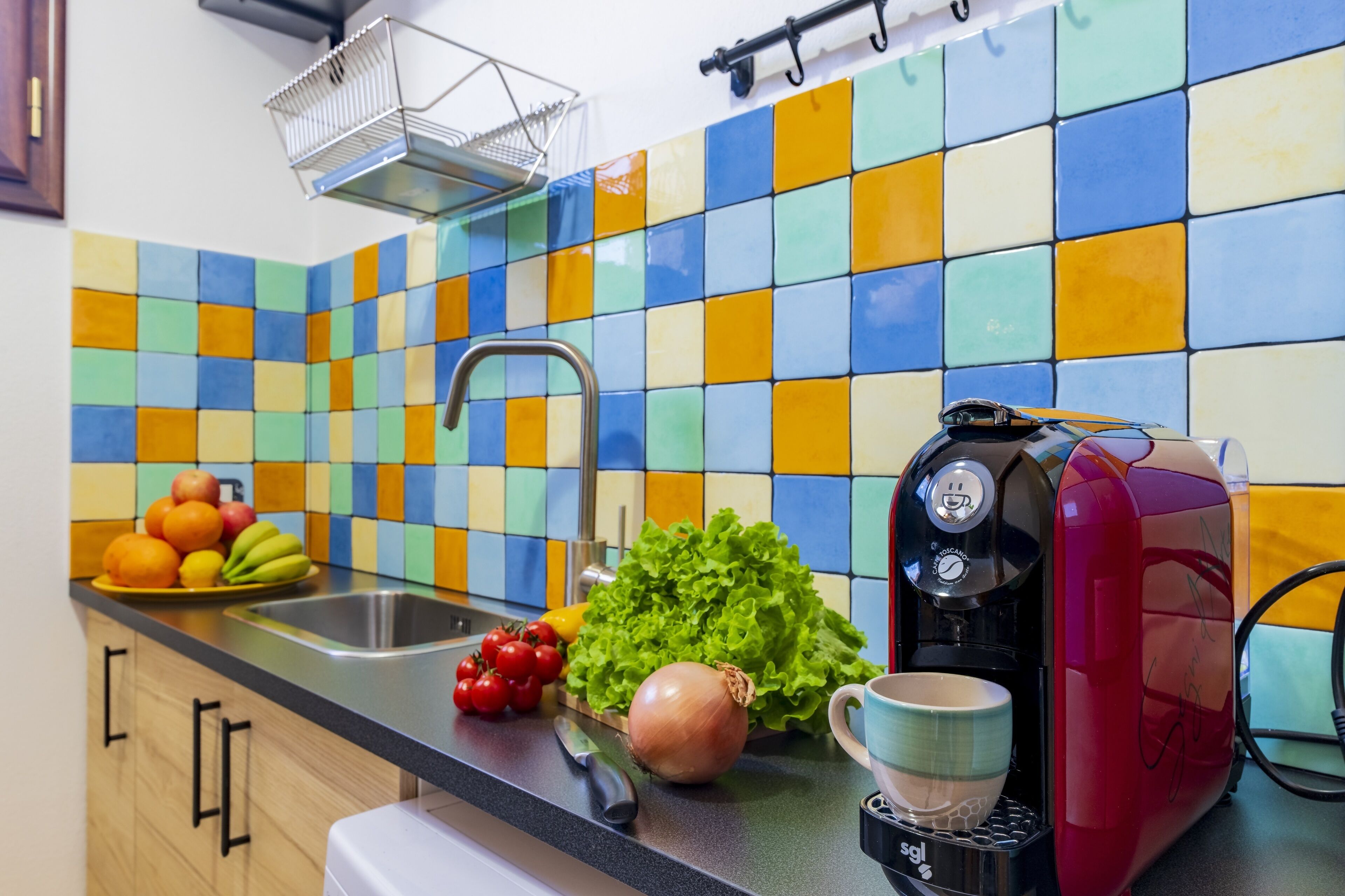 A kitchen with a colorful tile backsplash, a coffee maker, fresh produce, and a sink.