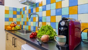 Una cocina con un colorido salpicadero de azulejos, una cafetera, productos frescos y un lavamanos.