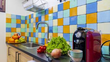A kitchen with a colorful tile backsplash, a coffee maker, fresh produce, and a sink.