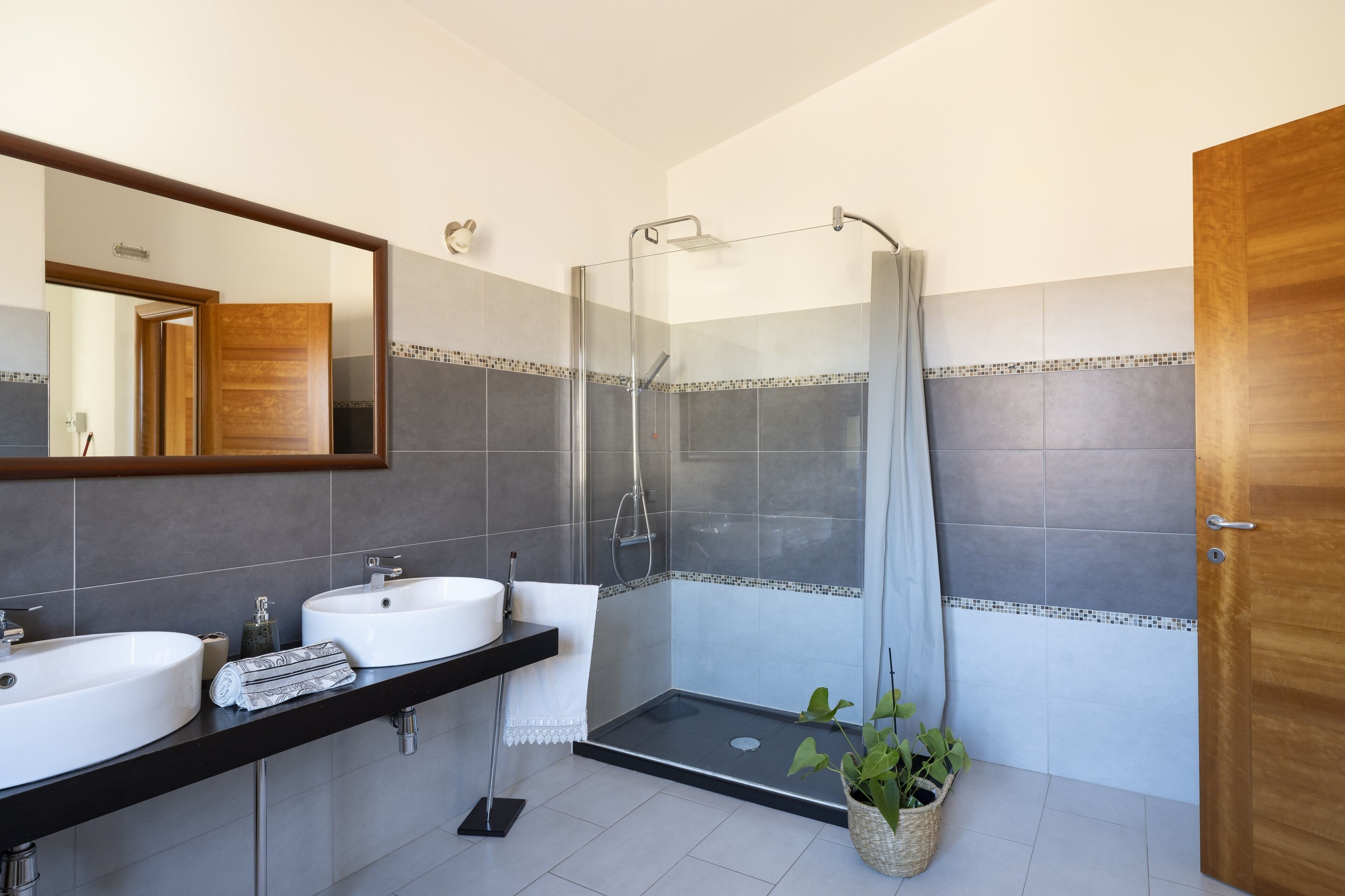 A modern bathroom with two sinks, a glass shower enclosure, and a wooden door.