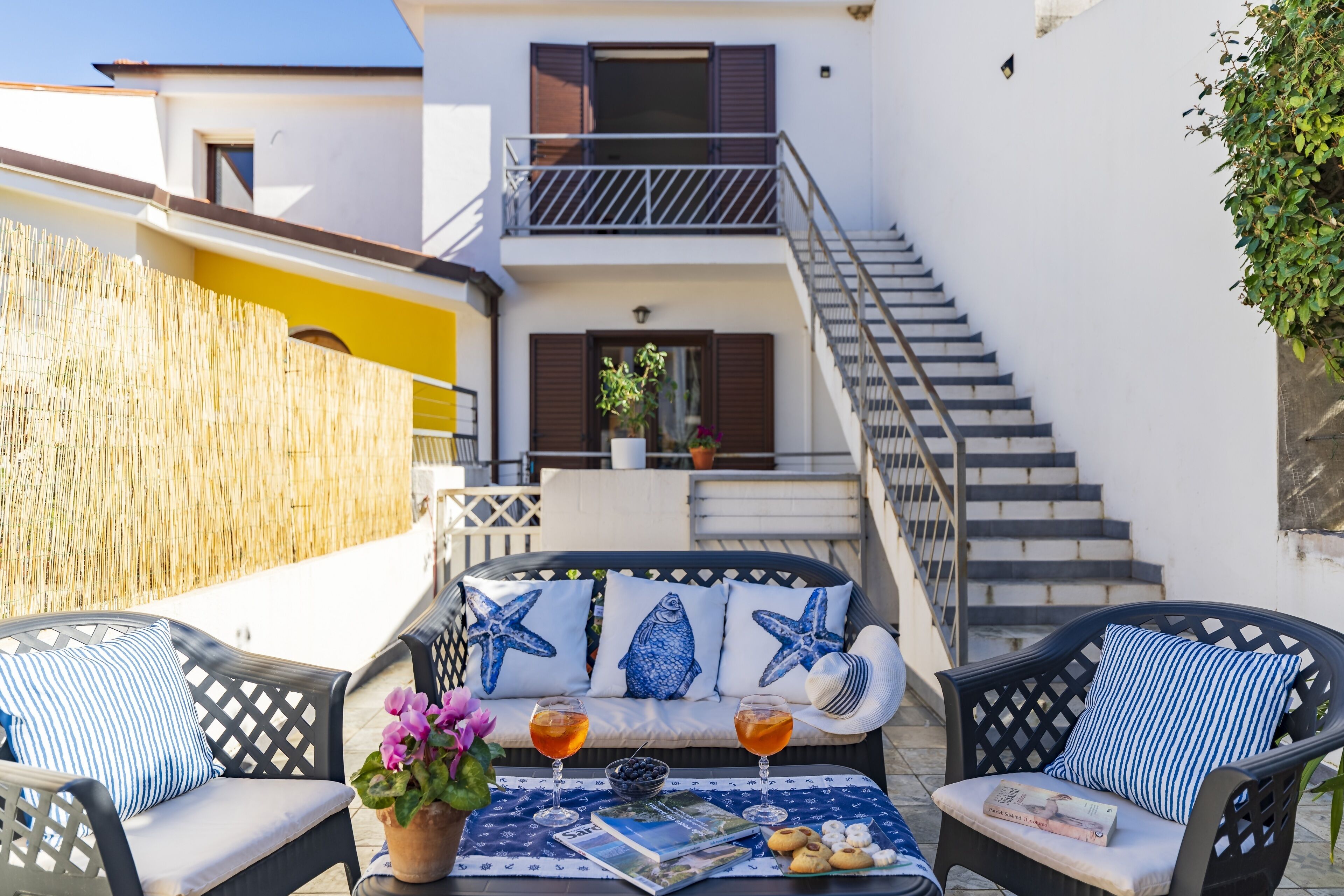 A terrace with outdoor seating, a table with drinks and snacks, and a staircase leading to an upper floor.