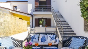 Una terraza con asientos al aire libre, una mesa con bebidas y aperitivos, y una escalera que lleva a un piso superior.