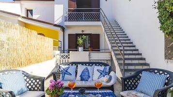 A terrace with outdoor seating, a table with drinks and snacks, and a staircase leading to an upper floor.