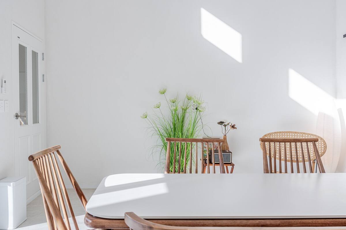 Un coin repas avec une table blanche et des chaises en bois, une plante en pot et une porte avec un interrupteur.
