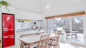 Een moderne keuken met witte kasten, een rode koelkast, en een eethoek met houten stoelen en een tafel.