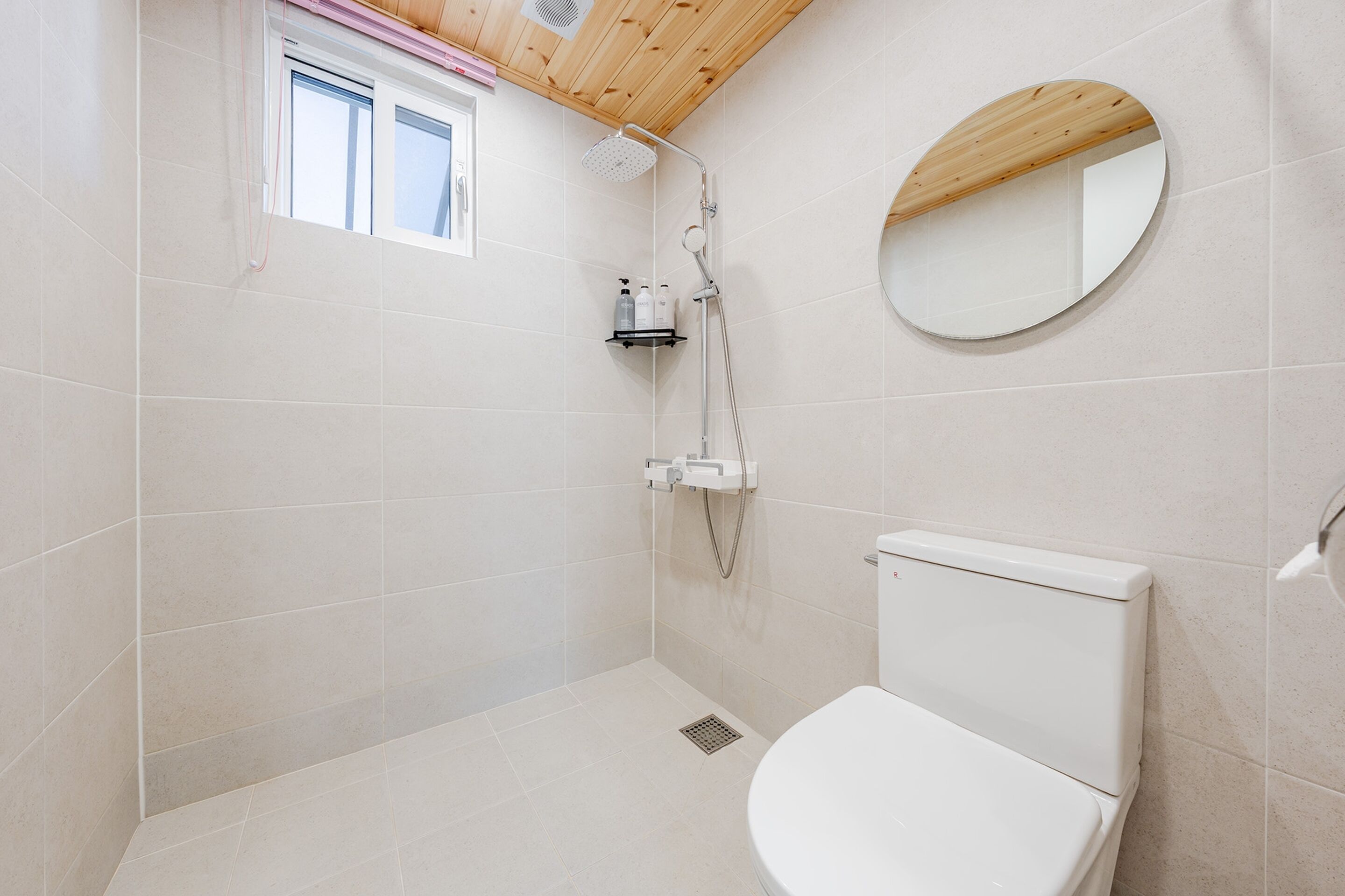 Une salle de bain avec une douche, des toilettes et un miroir rond au mur.