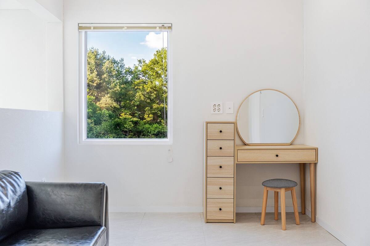 Une pièce minimaliste comprenant un bureau, une chaise et une grande fenêtre donnant sur des arbres.