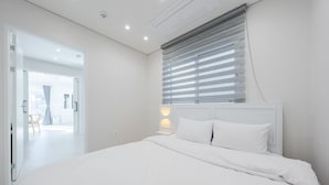 Een moderne slaapkamer met een groot bed, nachtkastje en een raam met zonwering.