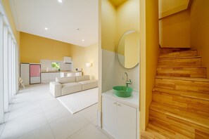 Een modern interieur met een keuken, een bank, een groene wastafel en een houten trap.