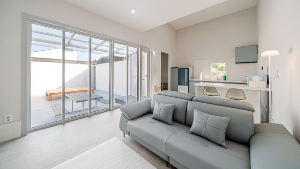 En moderne stue med en grå sofa, et fladskærms-tv og en skydedør, der fører ud til en balkon.