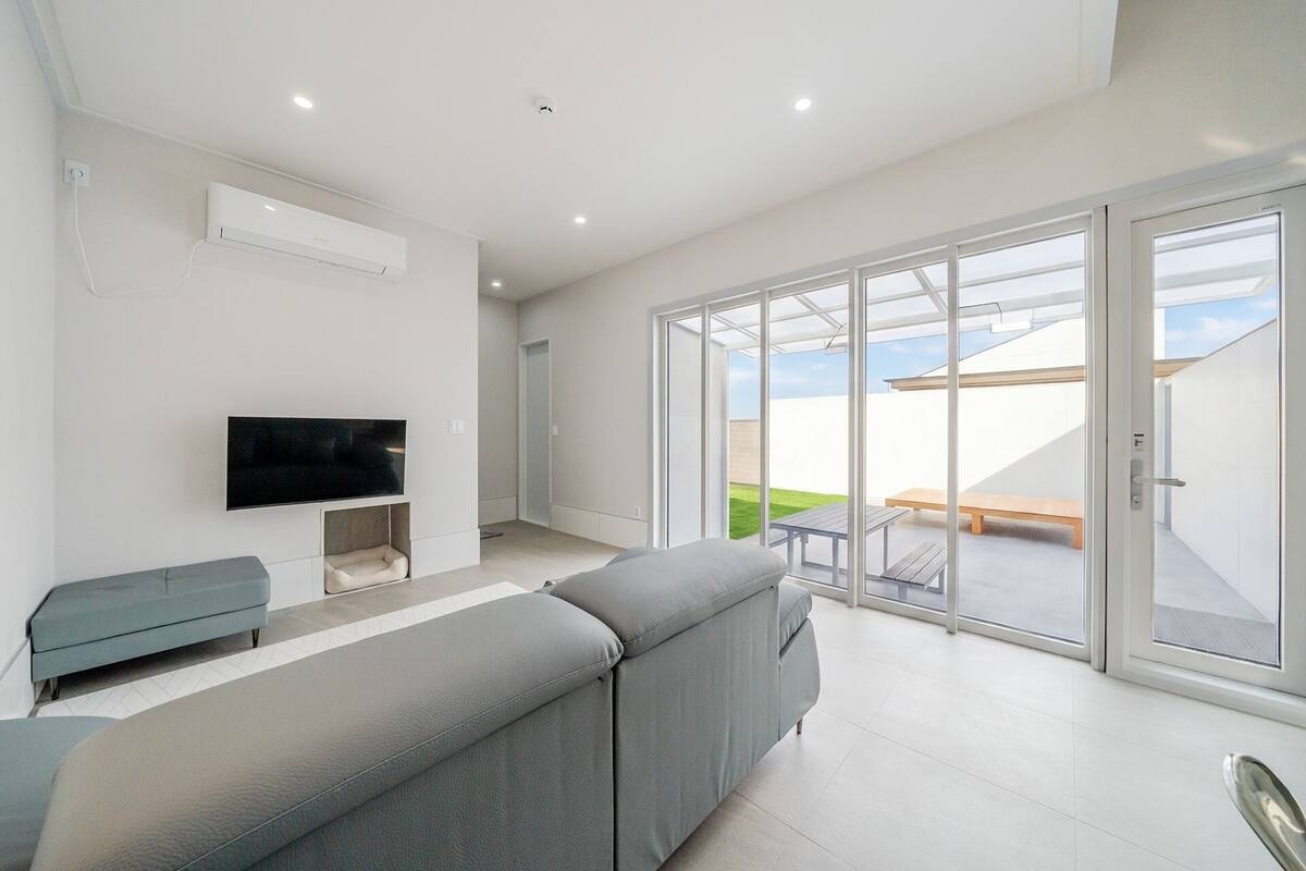 Una sala de estar moderna con un sofá gris, un televisor de pantalla plana y un ventanal corredero que da a un patio exterior.