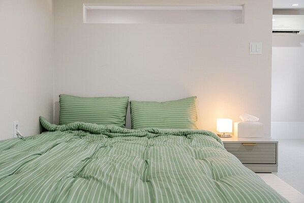 A neatly made bed with green striped bedding, a bedside lamp, and a nightstand with a tissue box. - Sokcho Hey My Green Private Pension (Sokcho)