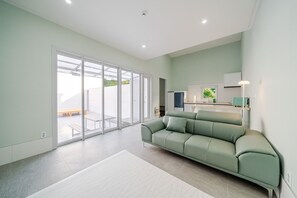 A modern living room with a sofa, a dining area, and a sliding glass door leading to an outdoor space. - Sokcho Hey My Green Private Pension (Sokcho)