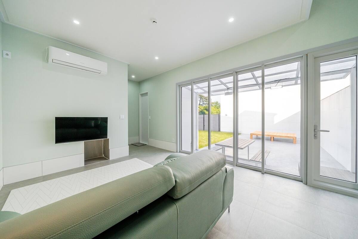 Una sala de estar moderna con un televisor de pantalla plana, un sofá y una puerta corrediza de vidrio que da a un patio con un banco.