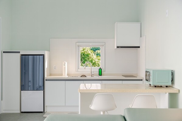 Una cocina moderna con ventana, un lavamanos, un refrigerador, un microondas y una zona de comedor con sillas.