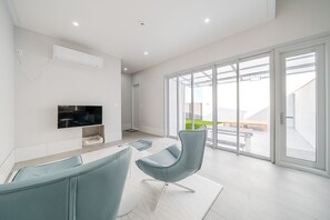 Een moderne woonkamer met een flatscreen televisie, een bank en een eethoek met een tafel en stoelen.