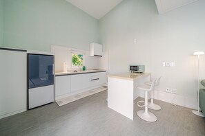 Een moderne keuken met witte kasten, een inbouwmagnetron en een klein barretje met witte barkrukken.