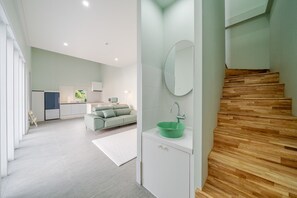 Un interior modern amb cuina, un sofà verd, una escala de fusta i un rentaplat blau verd.