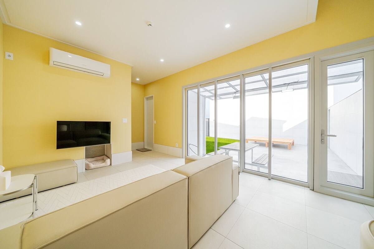 Un apartamento moderno con televisión de pantalla plana, sofá, cama y puerta de cristal corredera que da a un balcón.