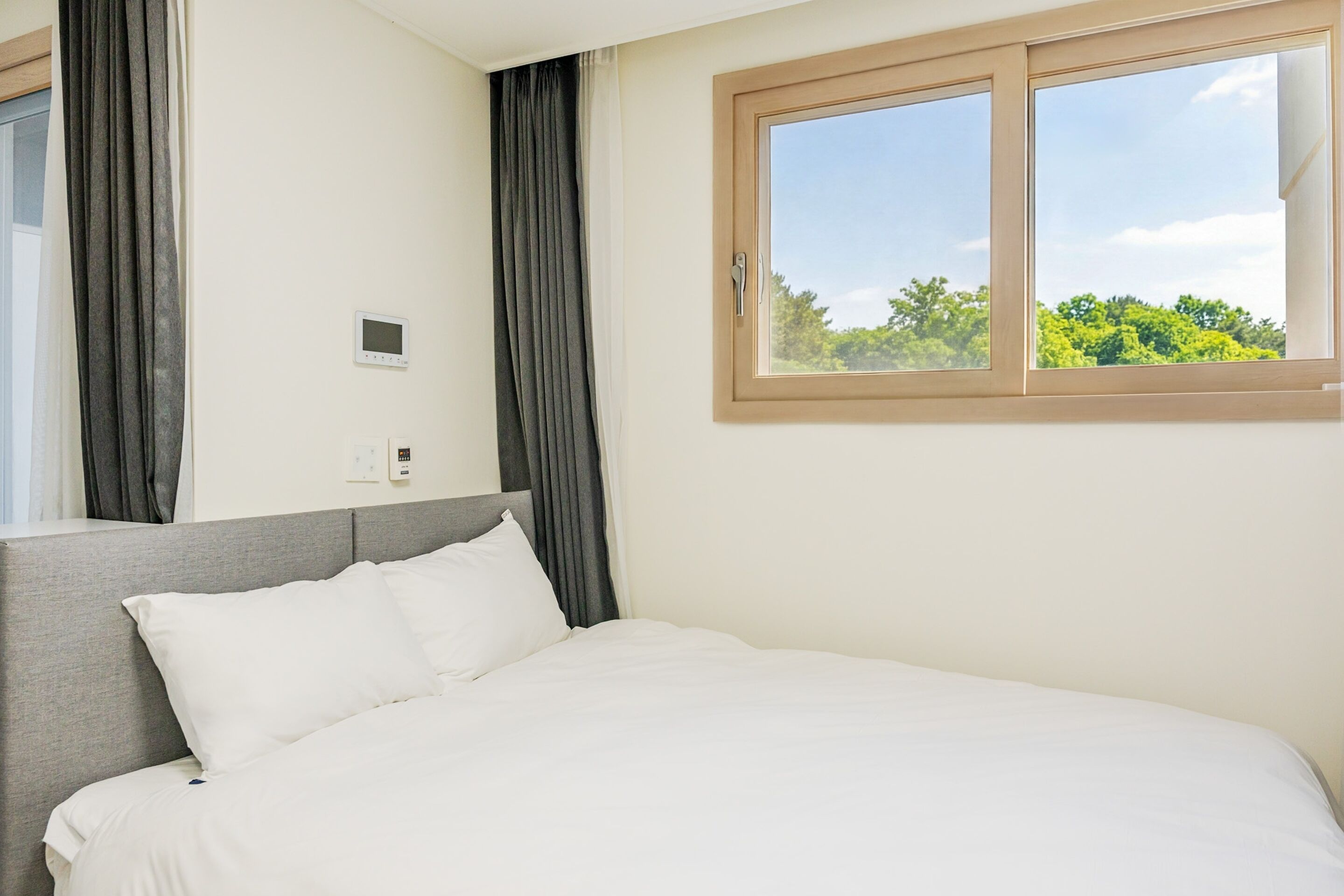 A hotel room with a bed, curtains, a window, and a thermostat.
