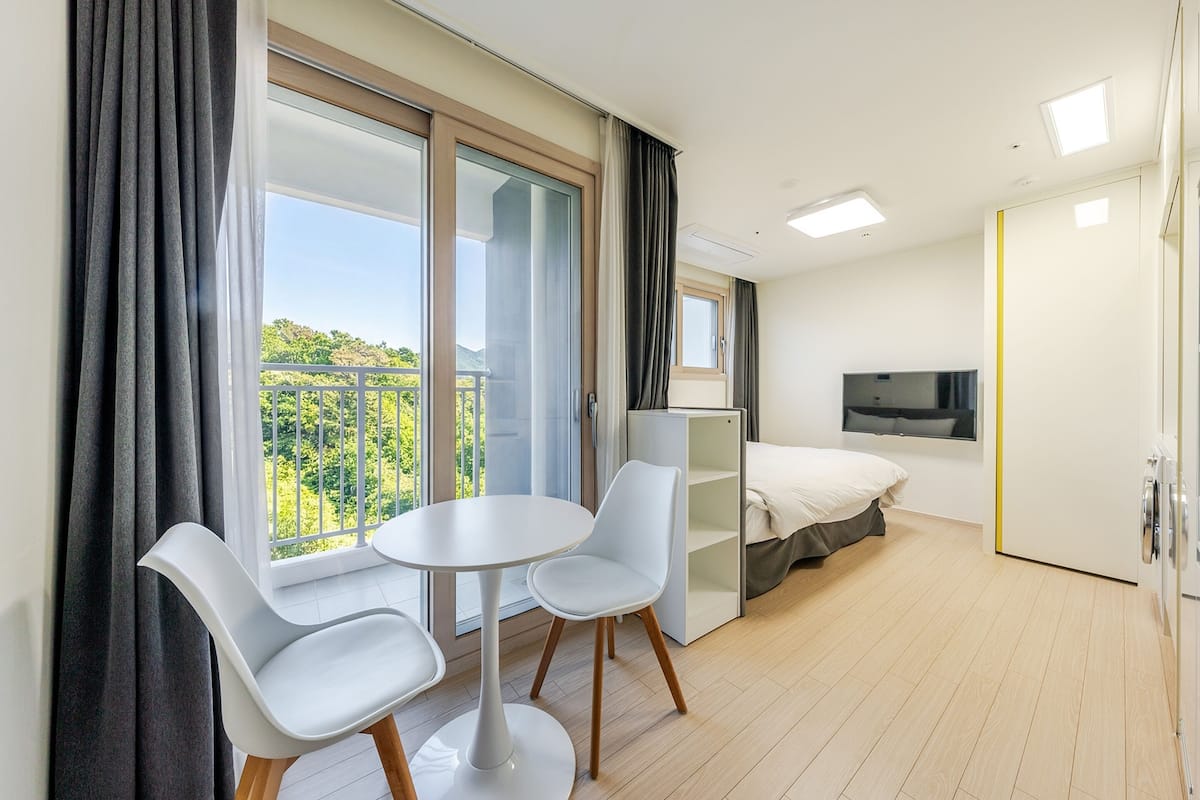 Et moderne hotelværelse med balkon, spiseplads med bord og stole, seng og fjernsyn.