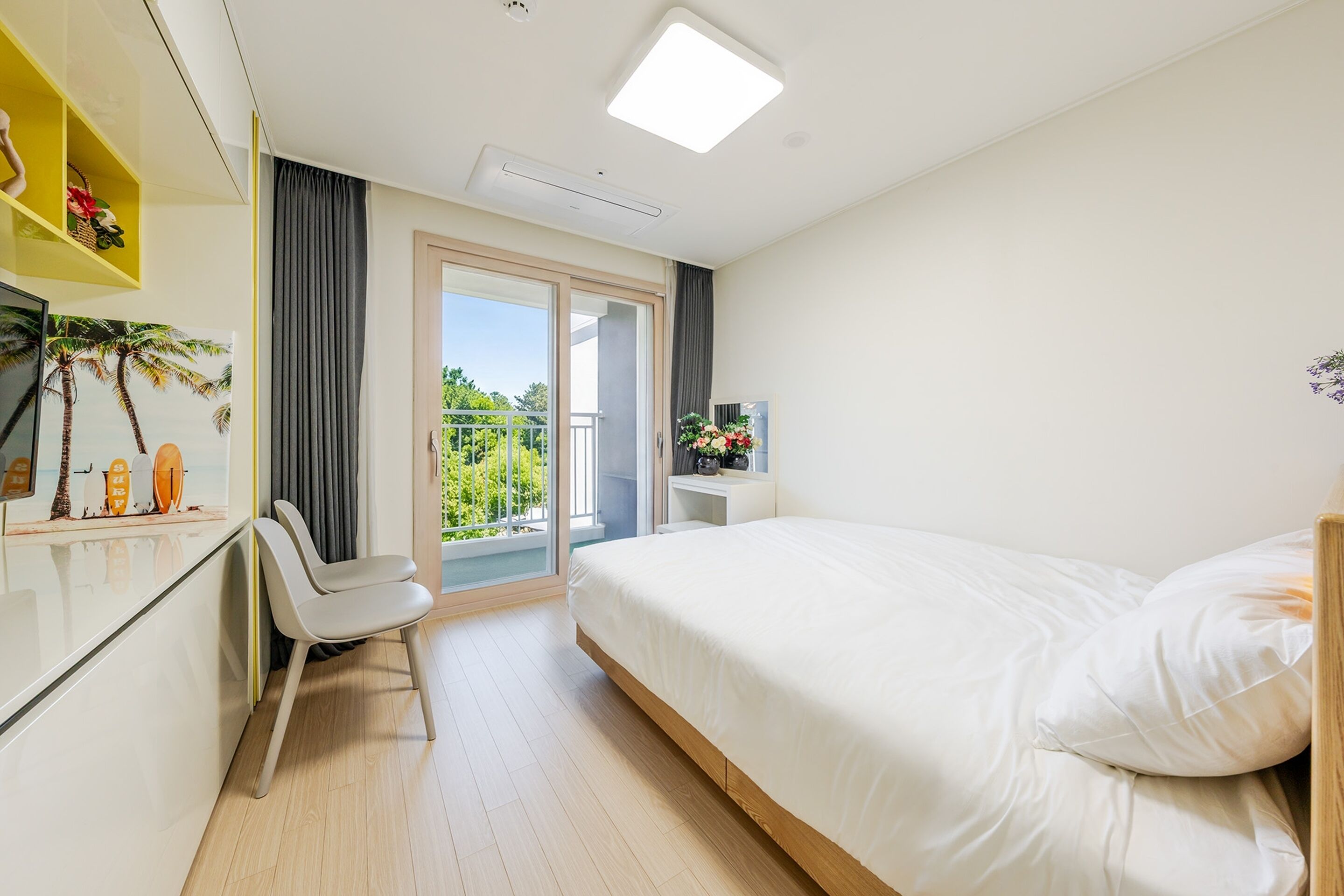 A hotel room with a bed, a desk, a chair, a TV, and a balcony with a view of greenery.