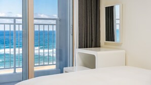 A hotel room with a large window overlooking the ocean, a white bed, a small desk, and a dark-colored curtain. - Yangyang Oceanstay 24K (Yangyang)