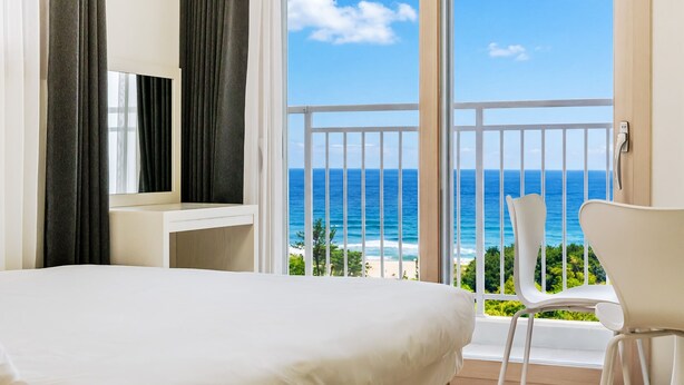 A hotel room with a large bed, a TV, a balcony with a view of the ocean, and a chair. - Yangyang Oceanstay 24K (Yangyang)