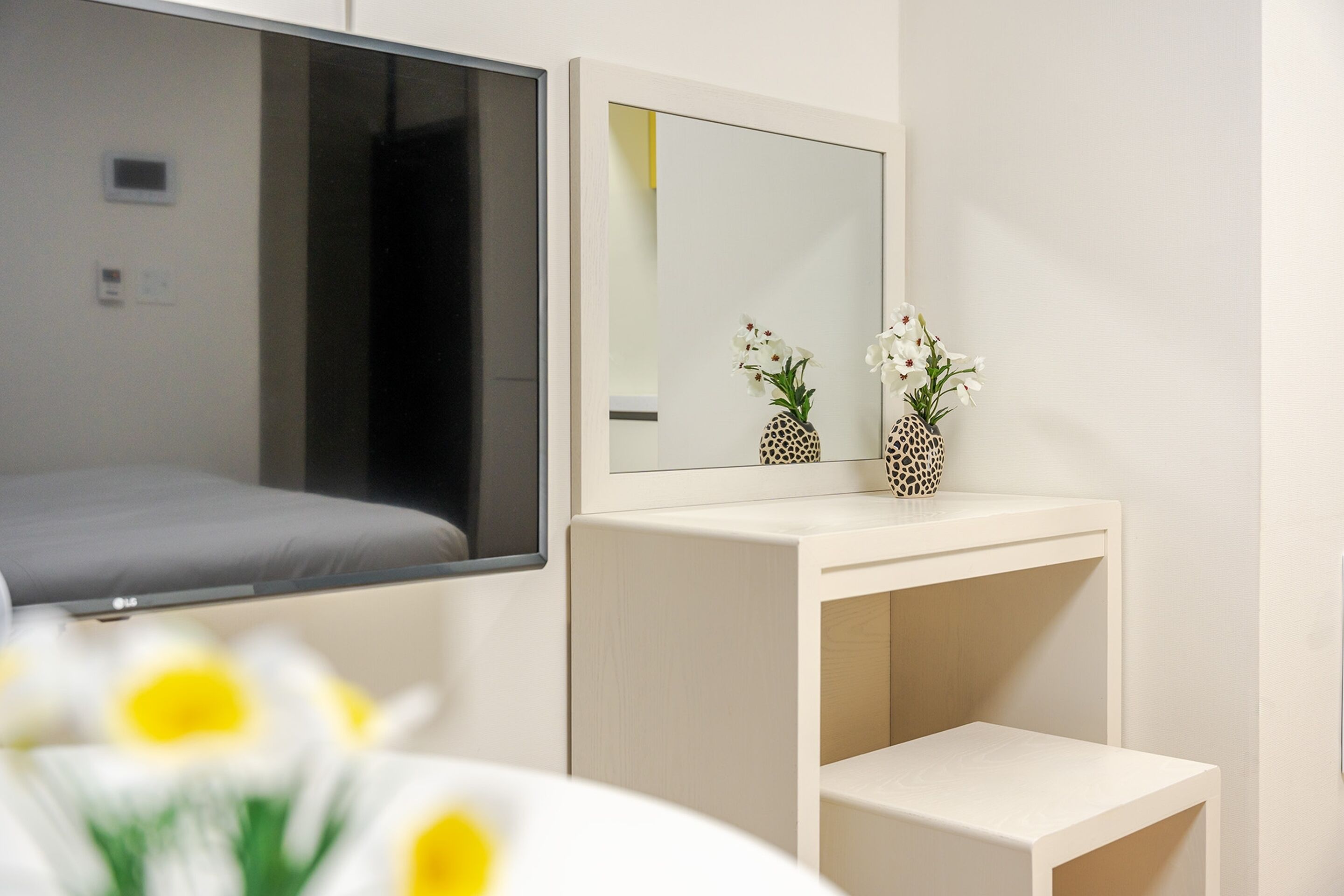 A hotel room with a bed, a bedside table, a mirror, and a small white cabinet.