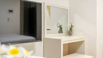 A hotel room with a bed, a bedside table, a mirror, and a small white cabinet.