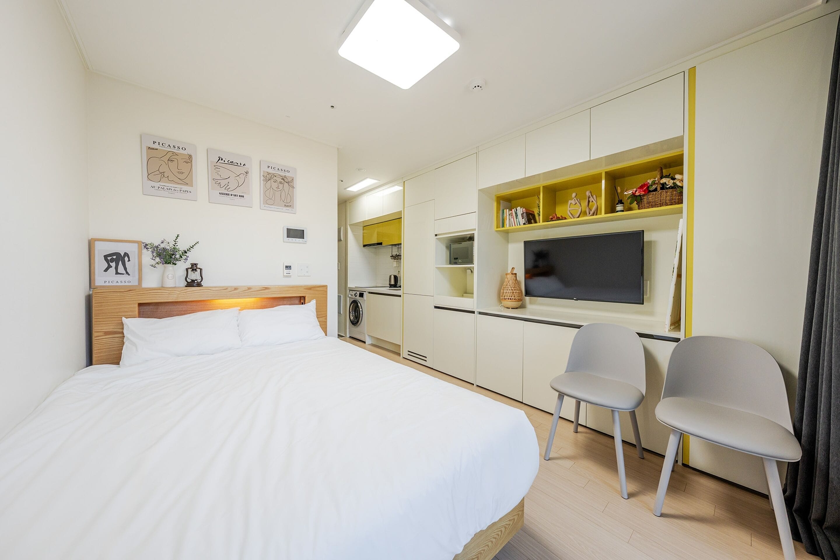A modern hotel room with a large bed, a desk, and a kitchenette.