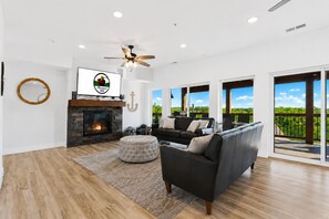 A spacious living room with a fireplace, a ceiling fan, and a large TV. - 9BR Table Rock Lake Lodge w/ Hot Tub & Game Room • Near SDC (Branson)