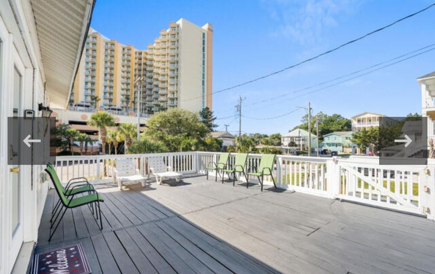 A wooden deck with outdoor seating, a white fence, and a view of tall buildings in the background.