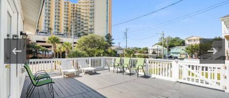 A wooden deck with outdoor seating, a white fence, and a view of tall buildings in the background.