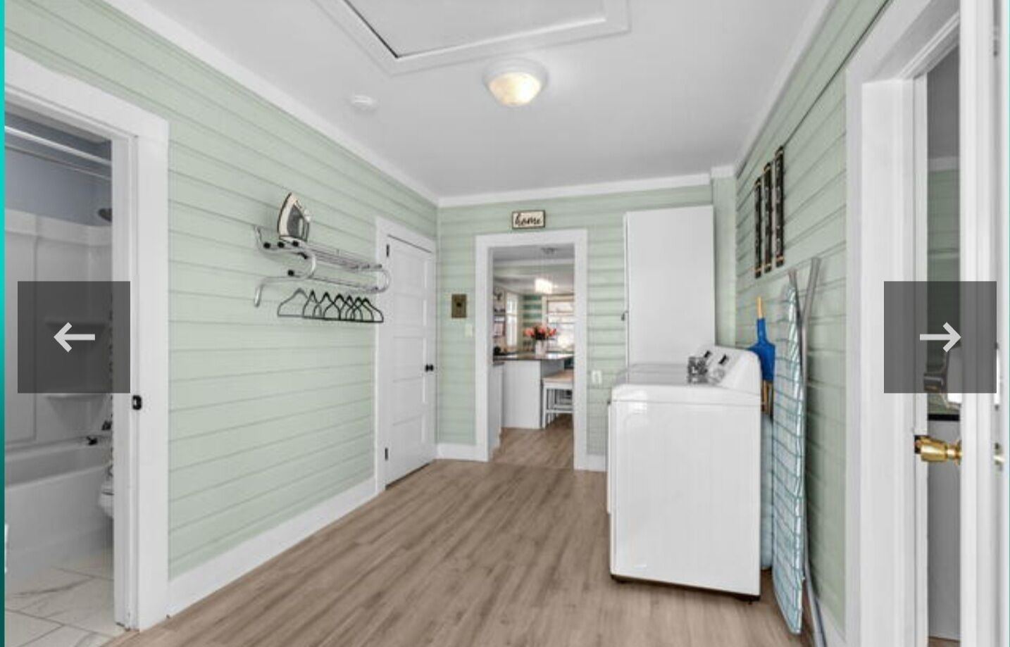 A laundry room with a washing machine, a drying rack, and a door leading to a kitchen area.