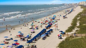 Een strand met rijen parasols en strandstoelen, een redershut en een uitzicht op de oceaan en de stadshemel op de achtergrond.