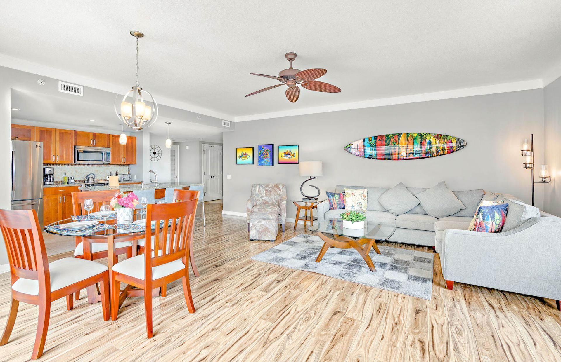 A modern living room with a dining area, kitchen, and a ceiling fan.