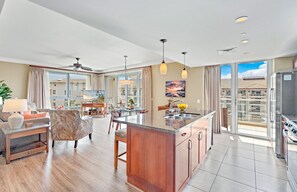 A modern kitchen with a central island, large windows, and a dining area with a view. - Maui Resort Rentals: Hokulani 605/6 –  4BR Retreat with Stunning 6th-Floor Ocean Views! (Lahaina)
